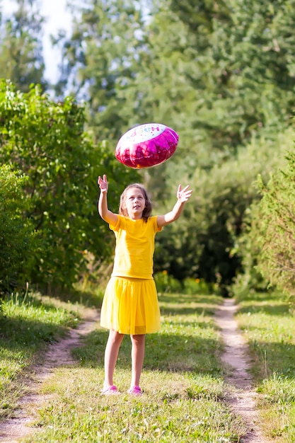 Adorable fille en robe jaune avec ballon coloré festif joyeux anniversaire en forme de fleur. Enfant heureux à l'extérieur