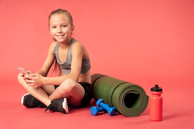 Adorable fille avec téléphone portable assis sur un équipement sportif soigné