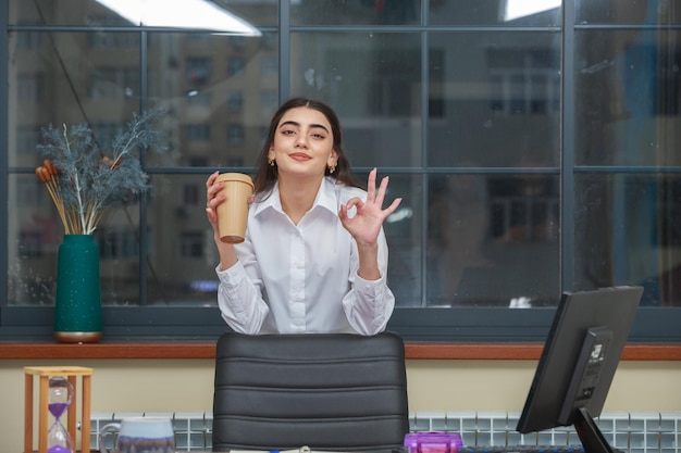 Adorable fille tenant une tasse de café et geste OK avec la main