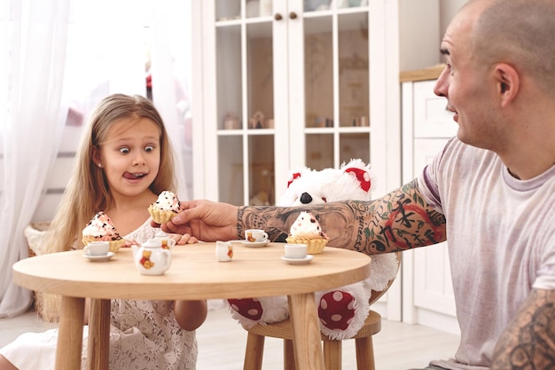 Adorable fille vêtue d'une robe blanche avec son père aimant, elles boivent du thé dans un dis...