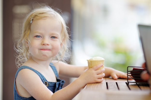 Adorable fillette mangeant des glaces dans un café en plein air