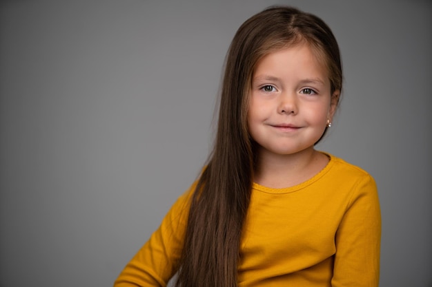 Adorable fillette de six ans isolée sur blanc joli enfant européen aux cheveux bruns pose un regard souriant à l'intérieur de la caméra