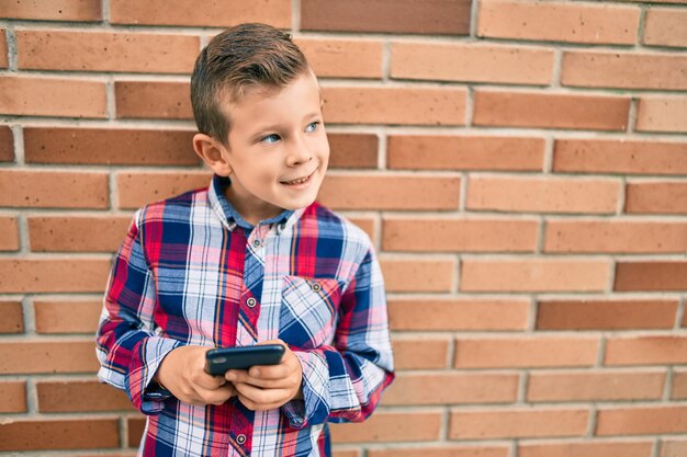 Adorable garçon caucasien souriant heureux en utilisant un smartphone dans la ville.