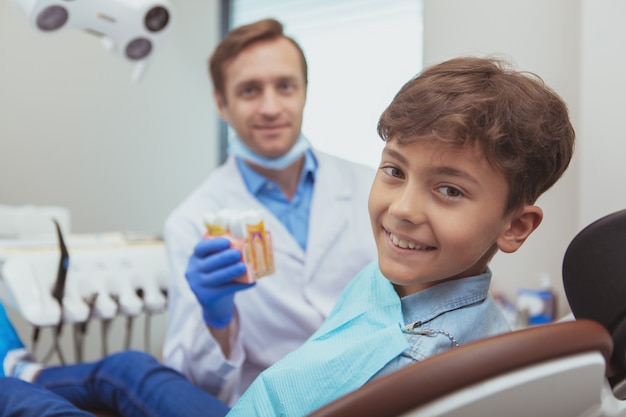 Adorable garçon heureux souriant à la caméra tout en étant assis sur une chaise de dentiste