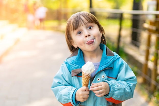 Adorable garçon mangeant de la crème glacée molle en plein air par temps de printemps ensoleillé Enfant souriant dans un parc avec un dessert sucré