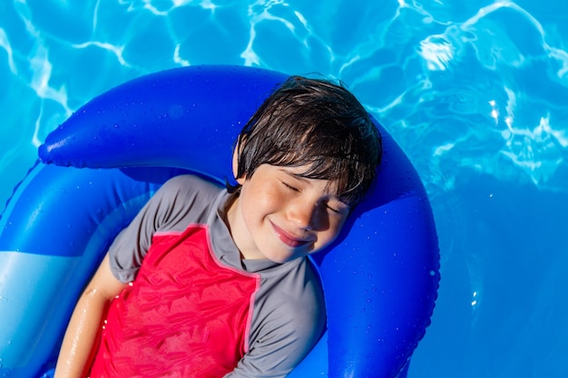 Adorable garçon se reposant dans la piscine sur un matelas gonflable