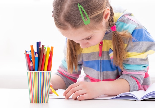 Adorable jeune élève travaillant soigneusement dans son cahier, sur fond blanc