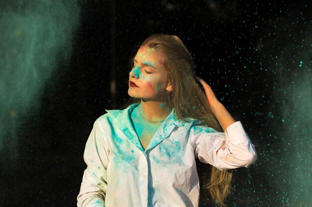 Adorable jeune femme aux cheveux rouges en chemise blanche posant avec de la peinture sèche Holi qui explose