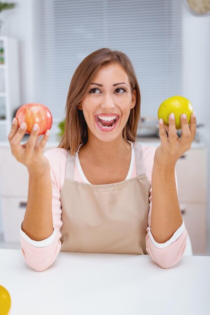 Adorable jeune femme à l'expression joyeuse, tient deux pommes fraîches, montre son petit-déjeuner,