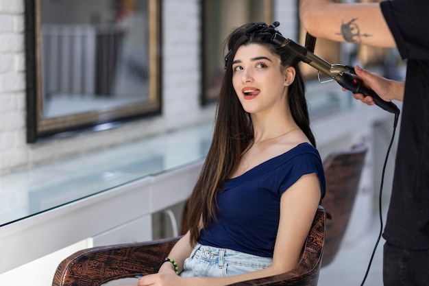 Adorable jeune fille assise sur la chaise et sort sa langue au salon de coiffure Photo de haute qualité