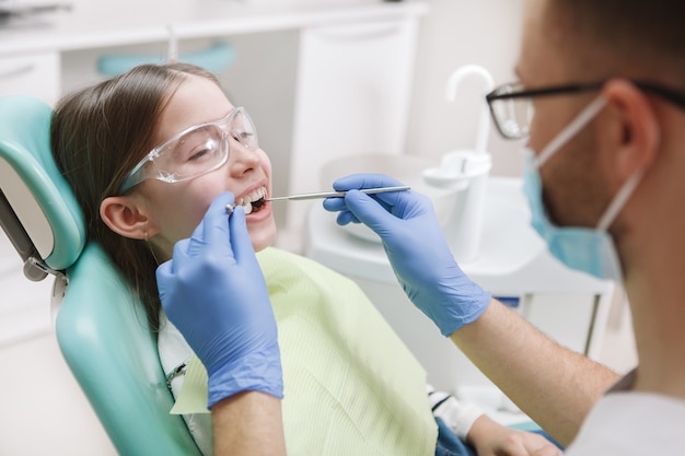 Adorable jeune fille heureuse souriant à son dentiste pendant le traitement des dents