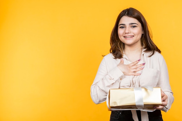 Adorable jeune fille tenant sa boîte-cadeau et posant sa main sur sa poitrine Photo de haute qualité