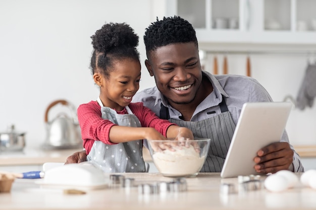 Adorable père et fille noirs cuisinant ensemble à l'aide d'une tablette numérique
