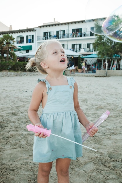 Adorable petit bambin s'amusant avec des bulles sur une plage de sable près de la maison en été