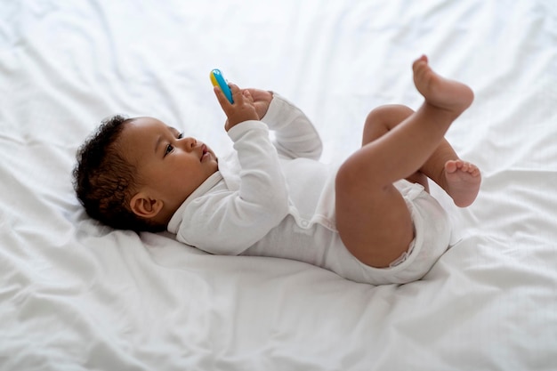 Adorable petit bébé noir allongé dans son lit et jouant avec un hochet