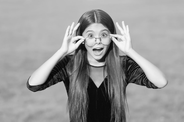 Adorable petit enfant avec un regard surpris et la bouche ouverte tenir des lunettes correctrices glissant vers le bas nez vert herbe été ensoleillé extérieur vue