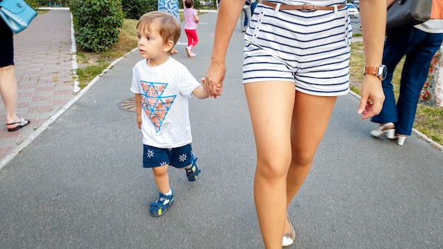 Adorable petit garçon de 3 ans tenant sa mère à la main et marchant dans la rue