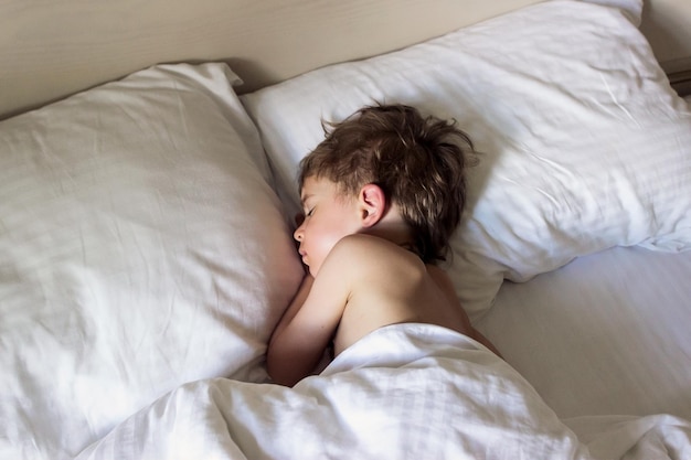 Adorable petit garçon en bas âge dormant dans un lit blanc L'enfant se repose ou fait la sieste Concept de confort Soft focus
