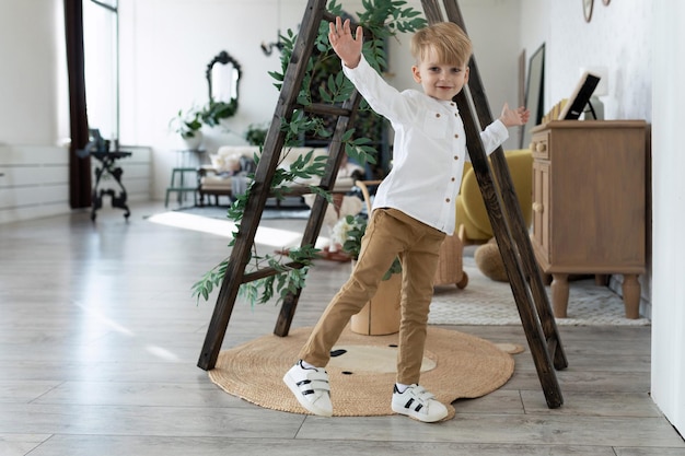 Adorable petit garçon en chemise blanche et pantalon beige regarde la caméra avec un sourire