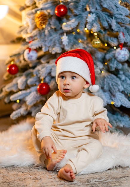 Adorable petit garçon dans une tenue de Noël assis sur une fausse fourrure douce devant un sapin de Noël Joyeux Noël et bonnes fêtes