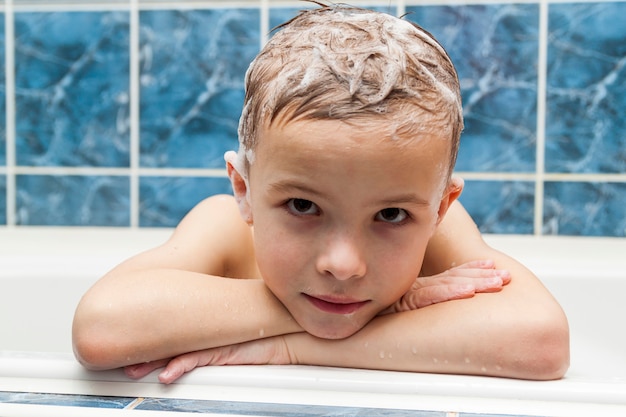 Adorable petit garçon avec de la mousse de savon au shampooing sur les cheveux en prenant un bain. Closeup portrait of smiling kid, concept de soins de santé et d'hygiène comme logo. Isolé sur fond blanc et bleu avec un tracé de détourage.