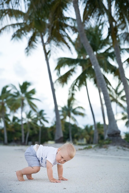 Adorable petit garçon rampant dans un parc tropical Mignon petit garçon apprenant à marcher dehors sur la plage de sable de l'océan Petit enfant près des palmiers