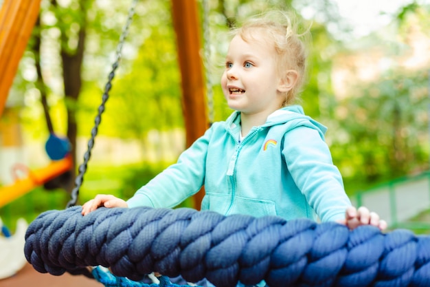 Adorable petite fille de 4 ans s&#39;amusant sur une balançoire en corde ronde dans une aire de jeux.