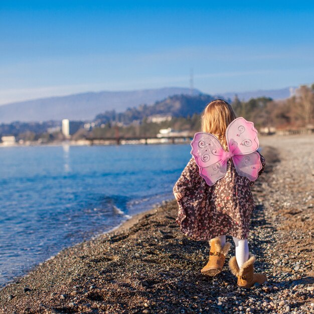 Adorable petite fille avec des ailes de papillon qui longe la plage dans une journée ensoleillée d'hiver