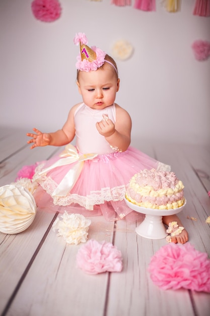 Adorable petite fille d'un an avec son premier gâteau d'anniversaire essayant du sucre et célébrant son anniversaire