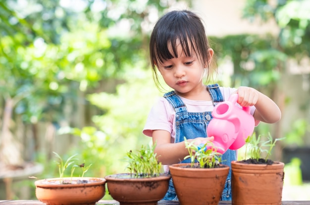 Photo adorable petite fille asiatique de 3 ans arrosant la plante dans les pots