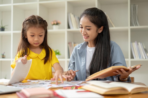 Une adorable petite fille asiatique d'âge préscolaire se concentre sur l'étude de l'anglais avec un gentil professeur privé