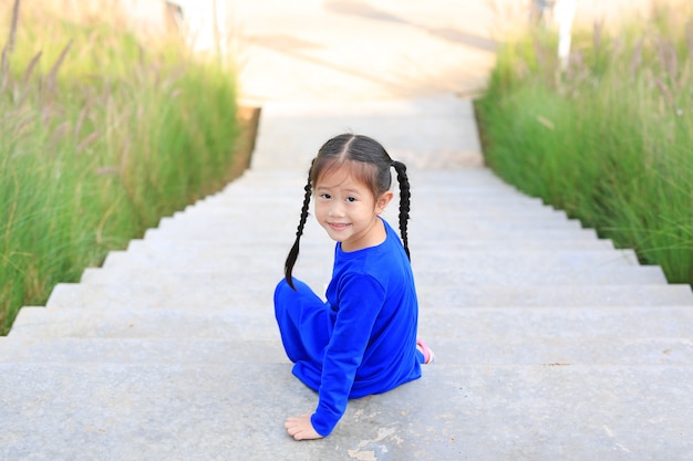 Adorable petite fille asiatique, assise sur un escalier dans le jardin avec caméra.
