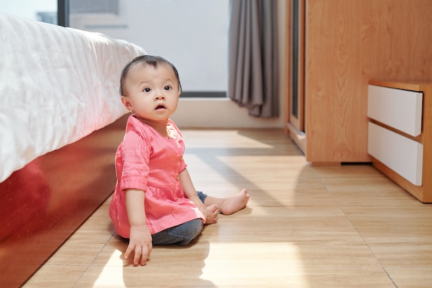 Adorable petite fille asiatique assise sur le sol dans la chambre de ses parents