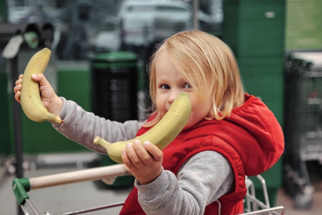 Adorable petite fille assise dans un panier dans un magasin de fruits alimentaires ou un supermarché Portrait petit enfant mignon faisant du shopping et achetant des fruits et légumes frais Nourriture saine pour le concept des enfants