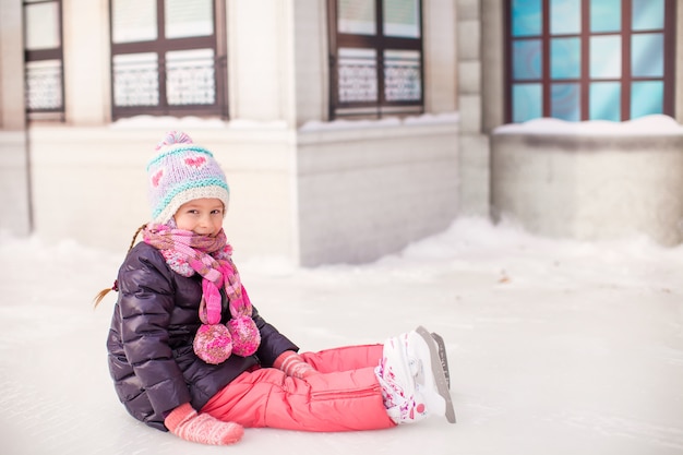 Adorable petite fille assise sur la glace avec des patins après la chute