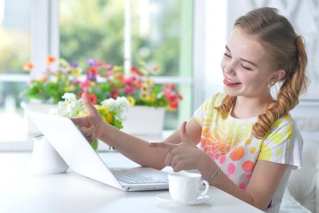 Une adorable petite fille assise à table avec un ordinateur portable à la maison