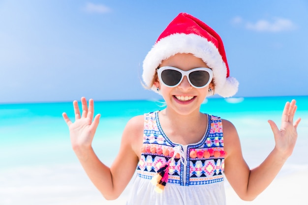 Adorable petite fille au bonnet de Noel pendant les vacances à la plage de Noël