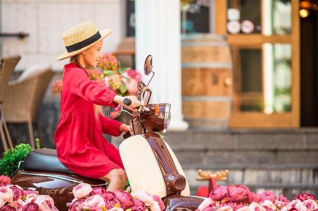 Adorable petite fille au chapeau sur le cyclomoteur à l'extérieur