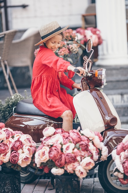 Adorable petite fille au chapeau sur le cyclomoteur à l'extérieur