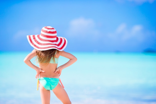 Adorable petite fille au grand chapeau marchant le long de la plage de sable blanc des Caraïbes