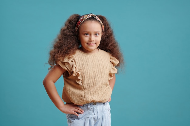 Adorable petite fille aux longs cheveux bruns ondulés qui vous regarde