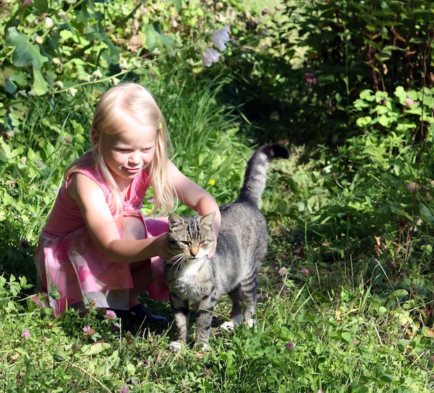 Adorable petite fille blonde jouant avec un chat dans le parc d'été