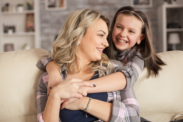 Adorable petite fille à bretelles ayant un grand sourire tout en serrant sa mère dans ses bras.