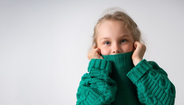 Adorable petite fille cachant la partie inférieure de son visage sous un col épais de chandail tricoté chaud.