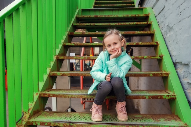 Adorable petite fille caucasienne assise sur l'escalier en fer avec intérêt en regardant les passants