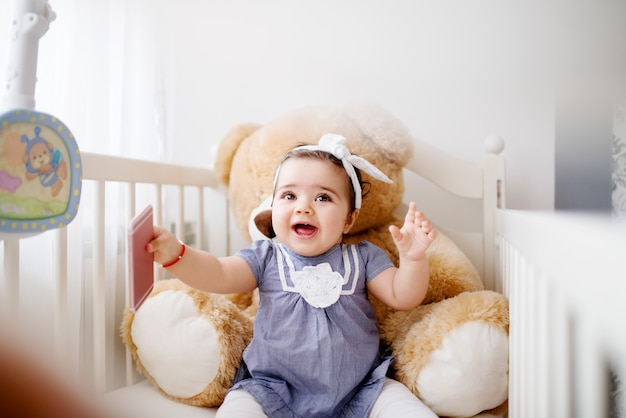 Adorable petite fille dans un berceau, jouant avec un téléphone intelligent.