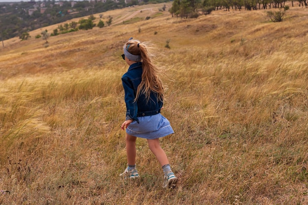 Adorable petite fille dans un chapeau de paille robe d'été à carreaux bleus dans la campagne de champ d'herbe Enfant avec une longue tresse blonde