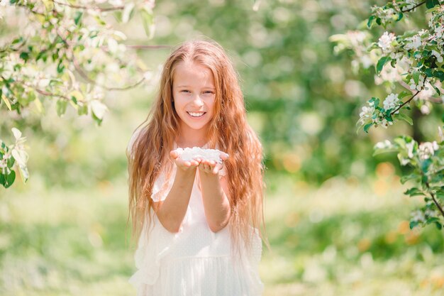 Adorable petite fille dans un jardin de pommes en fleurs sur une belle journée de printemps