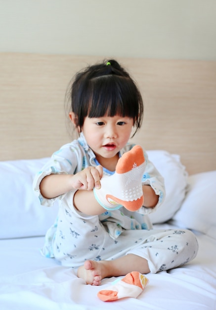 Adorable petite fille essayant de mettre des chaussettes sur le lit.