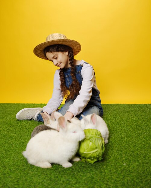 Adorable petite fille est allongée en train de jouer avec les lapins dans le fond jaune du studio